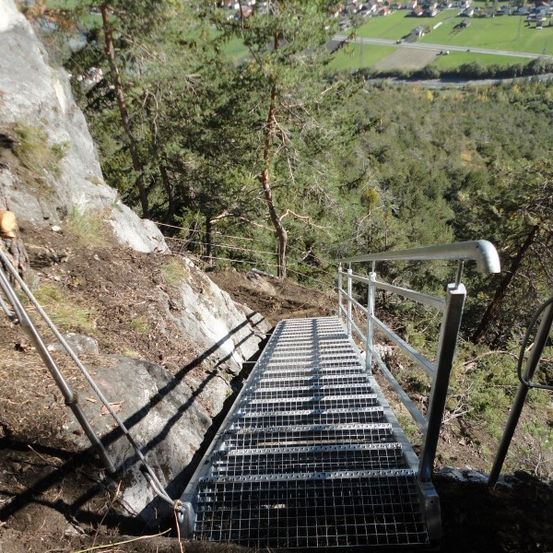 Eine Metalltreppe mit Handlauf ist an einem steilen Felsvorsprung befestigt und ermöglicht den Zugang zu einer höheren Ebene.