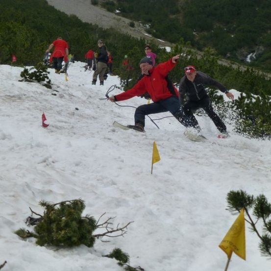Eine Gruppe von Menschen rutscht einen schneebedeckten Berg hinunter, angeführt von einem Mann in einem roten Mantel.
