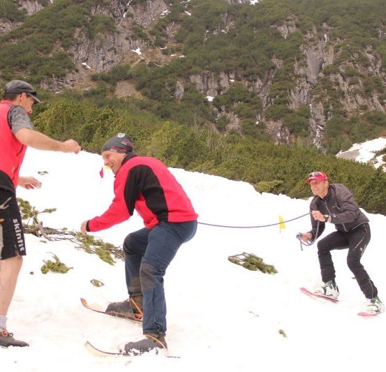 Drei Männer skifahren auf einem verschneiten Berg, wobei einer die anderen beiden mit einem Seil zieht.