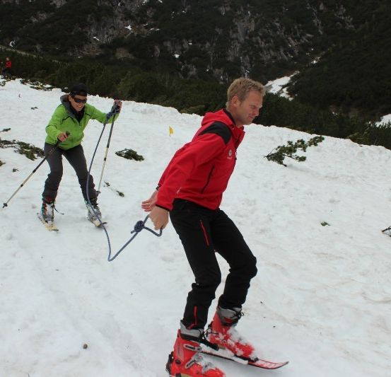 Eine Gruppe von Menschen skifahrert einen verschneiten Berg hinunter, wobei eine Person ein Seil hält.