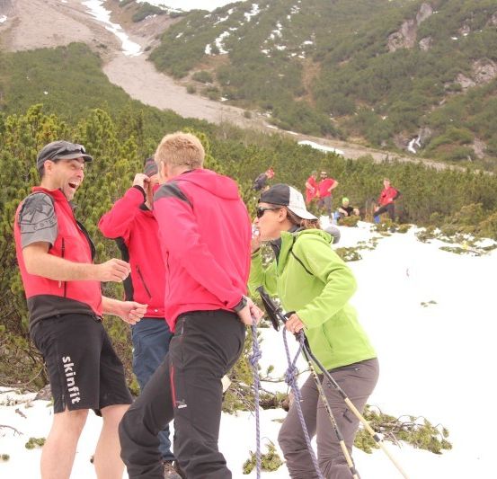 Eine Gruppe von Wanderern in roten und grünen Jacken steht auf einem verschneiten Berg, möglicherweise in einer Pause.