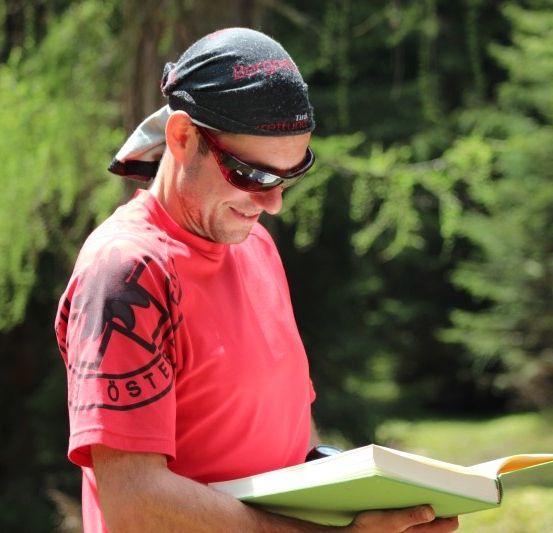 Ein Mann in einem roten T-Shirt und Sonnenbrille liest ein Buch im Wald.