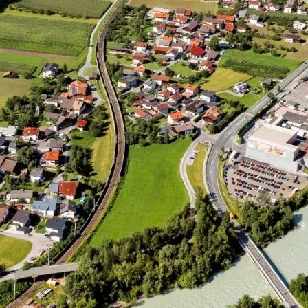 Luftaufnahme einer kleinen Stadt mit Häusern, einem Fluss und einer Straße. Die Stadt hat eine Mischung aus Wohn- und Geschäftsgebäuden, mit einem großen Gebäude auf der rechten Seite.