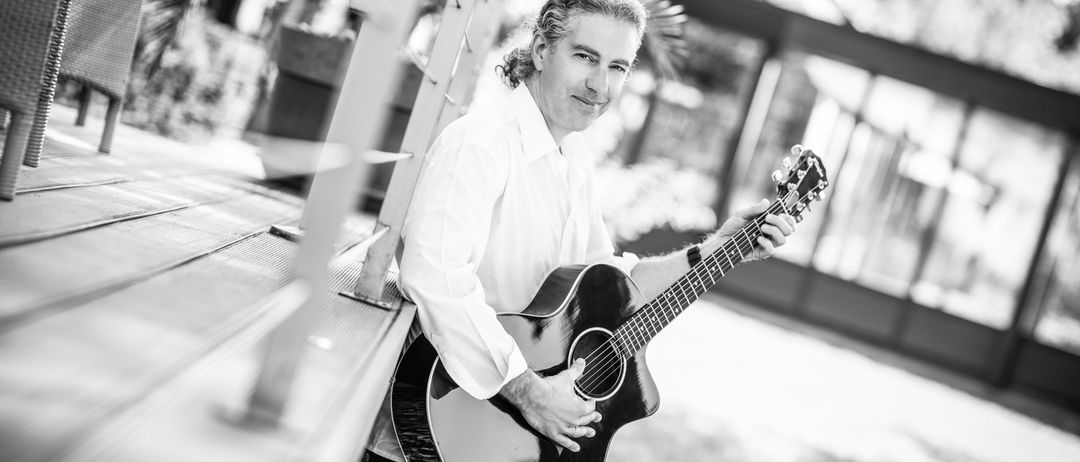 Ein Schwarz-Weiß-Bild eines Mannes, der eine Gitarre hält und lächelt, während er für ein Foto posiert.