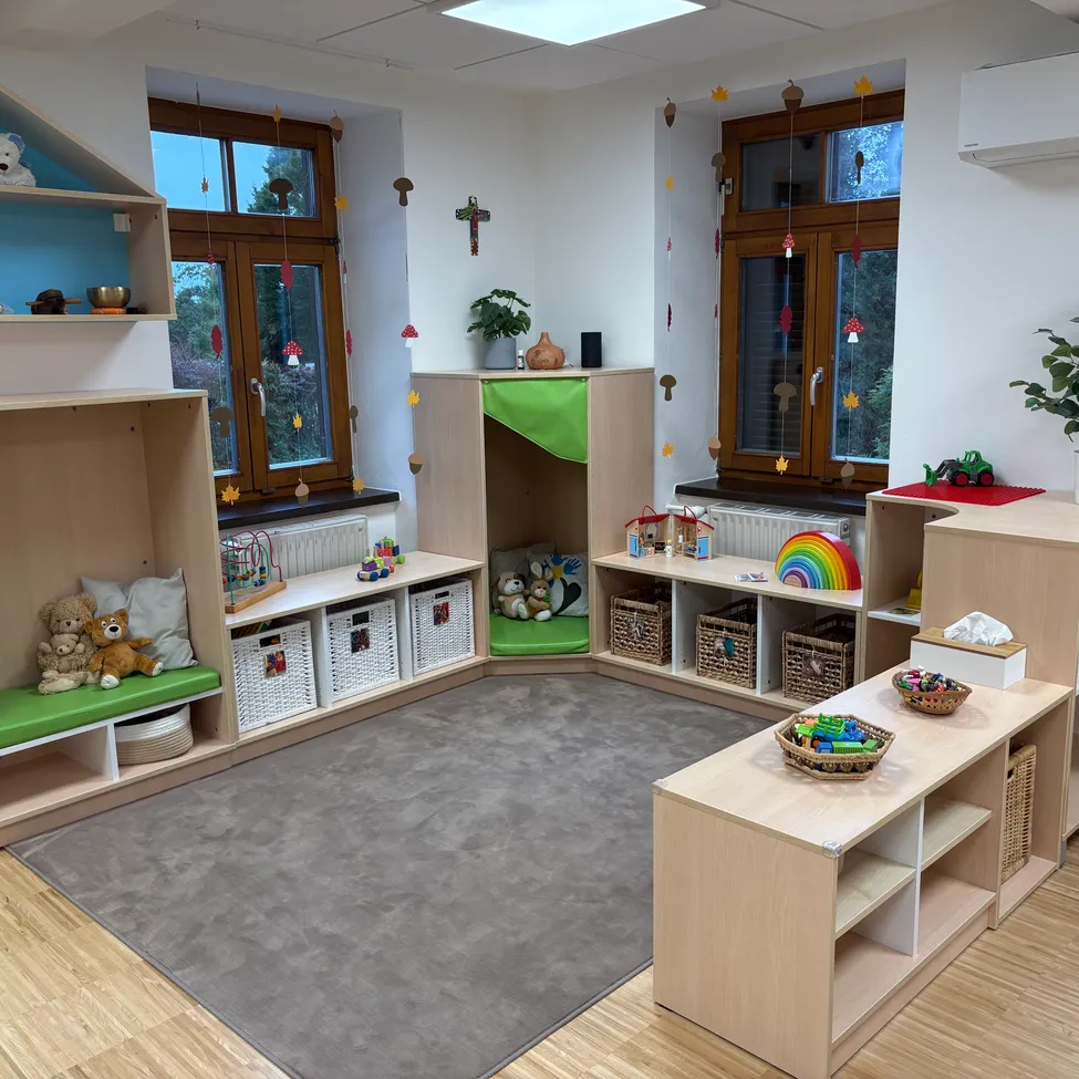 Ein gut organisiertes Spielzimmer mit Holzregalen, Teppich und Spielzeug. Fenster mit Dekorationen und Pflanzen sorgen für eine fröhliche Atmosphäre.