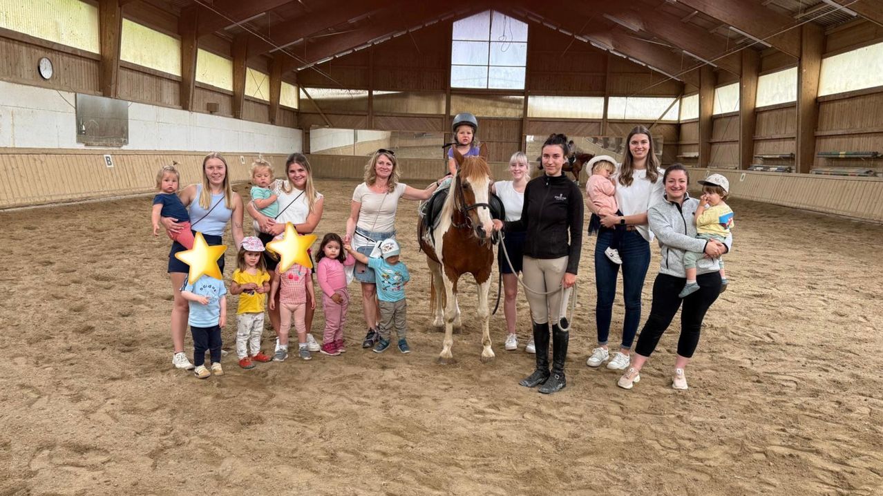 Eine Gruppe von Frauen und Kindern, einschließlich eines Kleinkindes auf einem Pferd, posiert für ein Foto in einer überdachten Reithalle. Einige tragen Hüte, und einige halten Säuglinge.