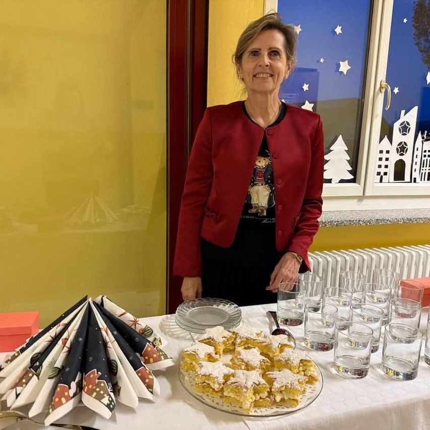 Eine Frau steht neben einem Tisch mit Dessert und Servietten. Hinter ihr zeigt ein Fenster Weihnachtsdekorationen.