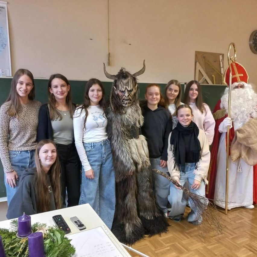 Eine Gruppe junger Frauen und eine Person in einem Hörnerkostüm posieren für ein Foto mit einer als Weihnachtsmann verkleideten Person.