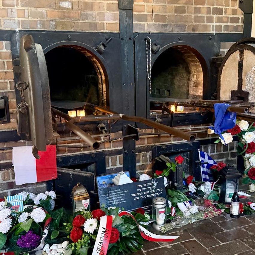 An Ziegelwand hält zwei große Öfen mit offenen Türen. Kerzen und Blumen stehen vor den Öfen, zusammen mit einigen Flaggen.