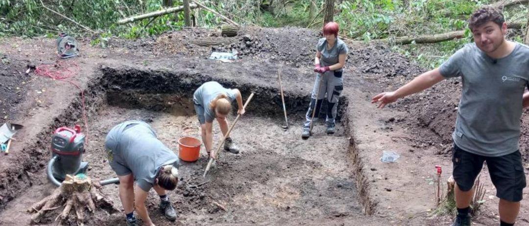 Drei Personen graben im Boden. Eine hält eine Schaufel, eine andere einen Eimer, und die dritte beobachtet. Der Boden ist braun und hat einige Spuren. Unten steht das Wort 'KICK-OFF'.
