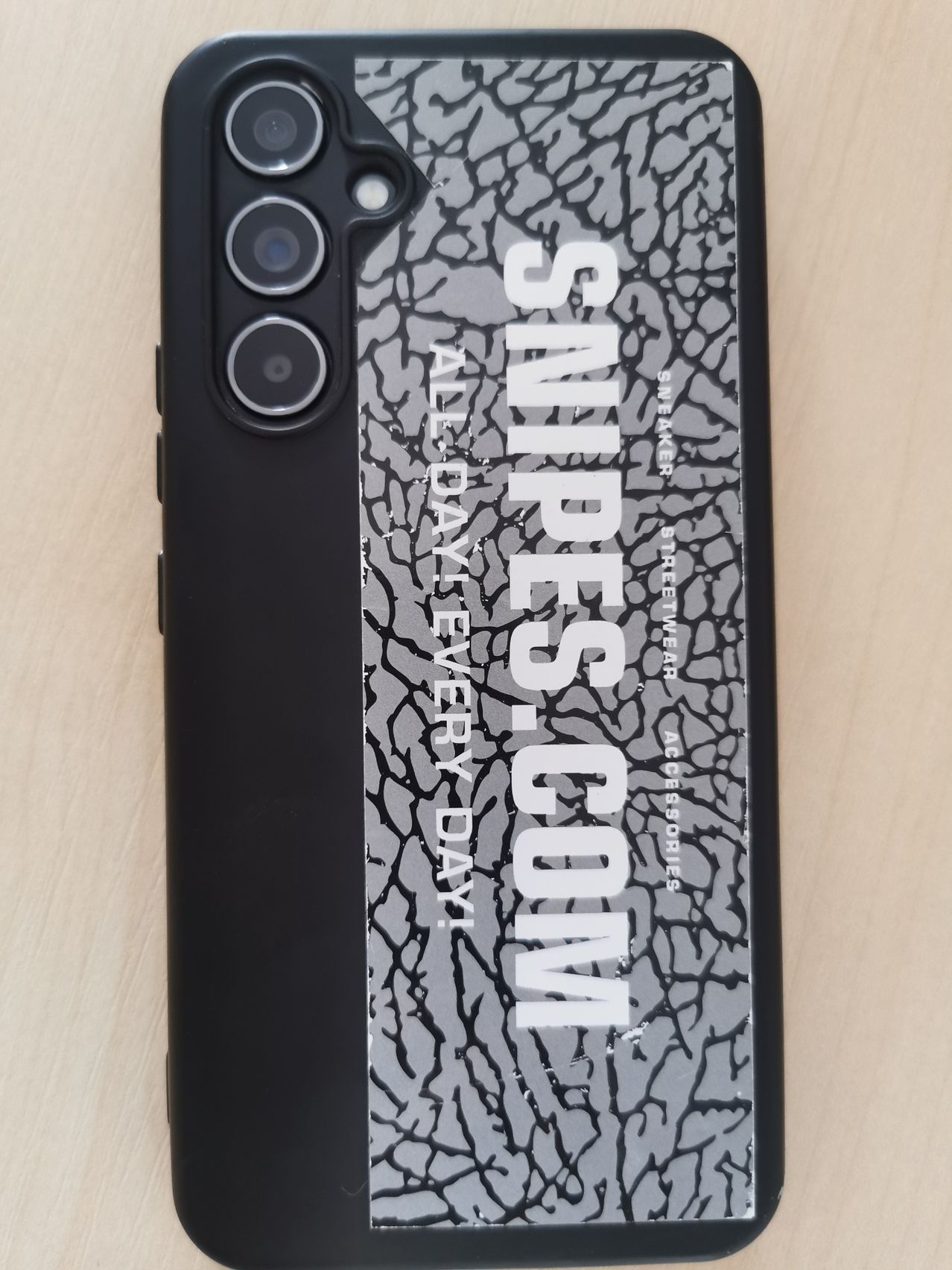 Eine schwarze Smartphone-Hülle mit rissiger Struktur. Es steht 'SUPRES.COM' und 'ALLE TAG JEDEN TAG' in Weiß. Der Hintergrund ist eine Mischung aus Grau und Schwarz.