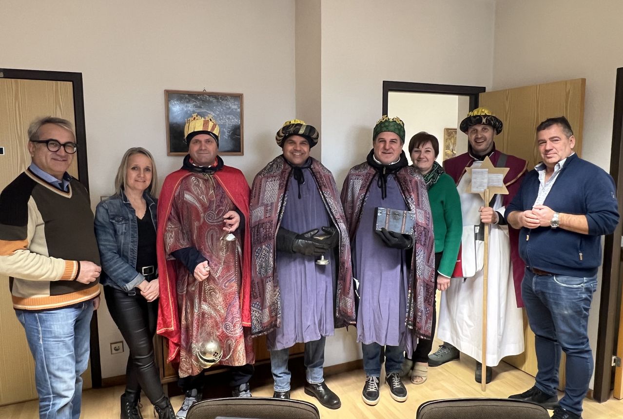 Eine Gruppe von Menschen in mittelalterlichen Kostümen steht in einem Raum und lächelt für ein Foto. Drei Männer tragen Kronen, während die Frau in Lederhosen neben ihnen steht.