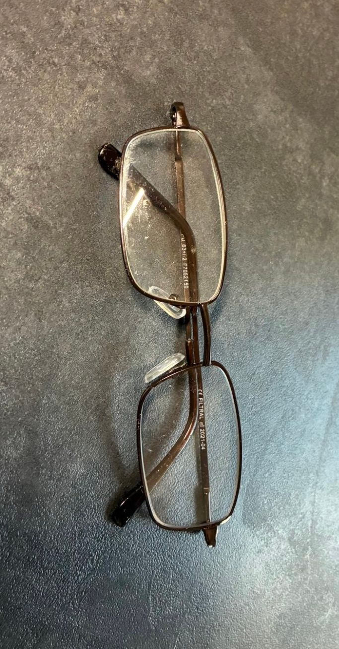 Ein Paar Brille mit braunen Bügeln und klaren Gläsern liegt auf einer grauen Oberfläche. Die Gläser haben eine Lichtreflexion.