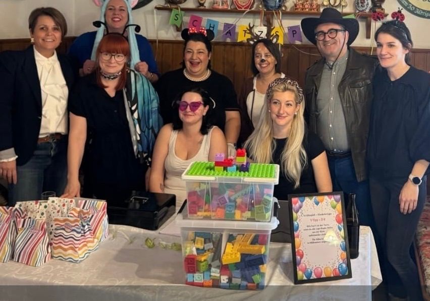 A group of people dressed in costumes and masks are posing for a photo with a table of gifts and a Lego structure.
