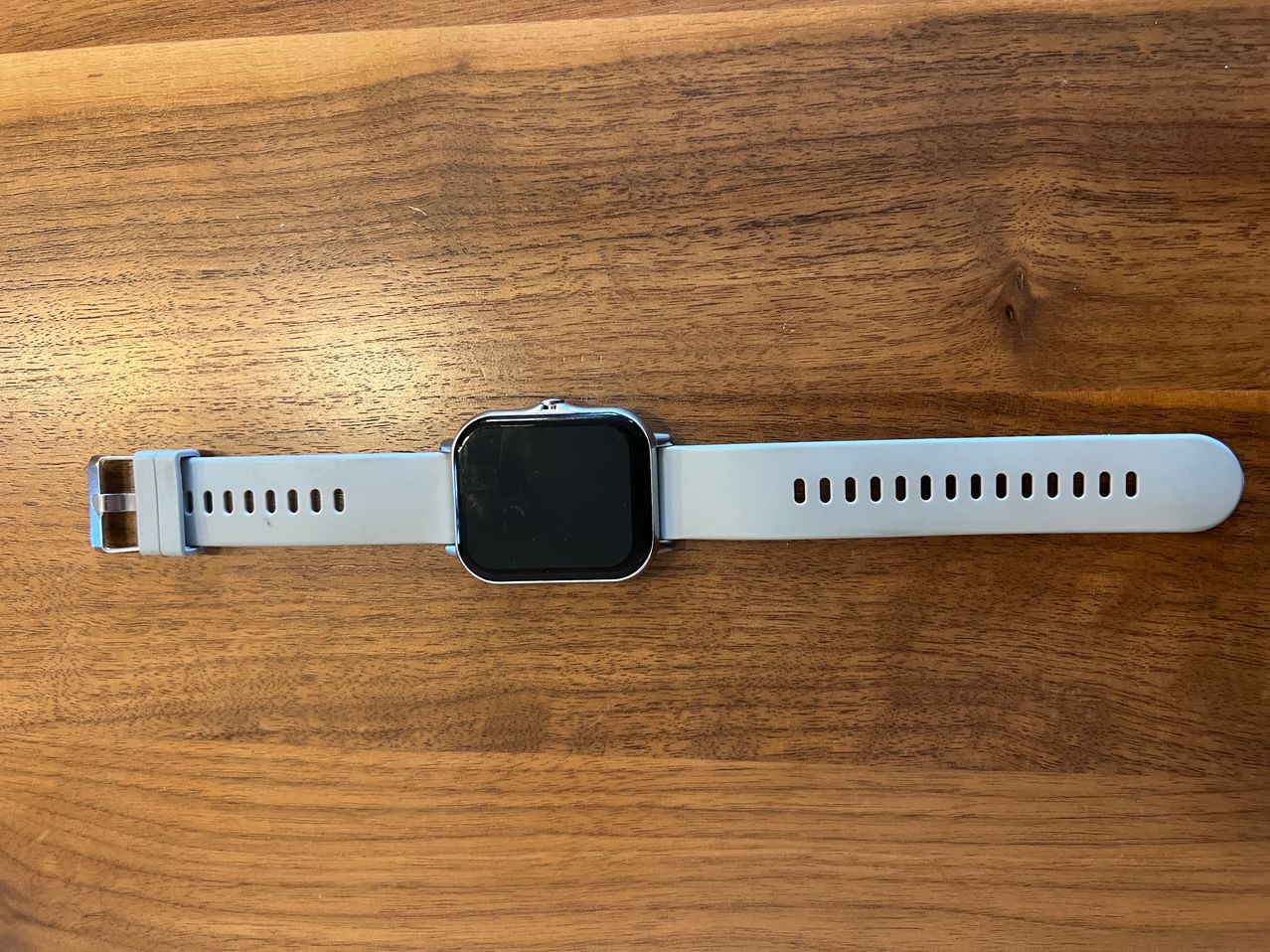 Eine weiße Smartwatch mit schwarzem Bildschirm und weißem Armband liegt auf einer Holzoberfläche.