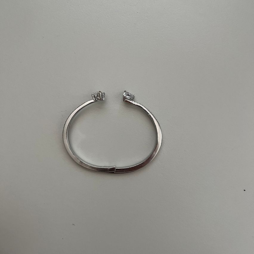 Eine silberne Armspange mit zwei kleinen Diamanten auf den Seiten liegt auf einem grauen Hintergrund.