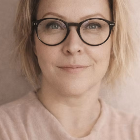 Eine Frau mit Brille und blonden Haaren lächelt in die Kamera, mit dem Wort 'Herz' in kursiver Schrift darüber. Der Hintergrund ist hellrosa.
