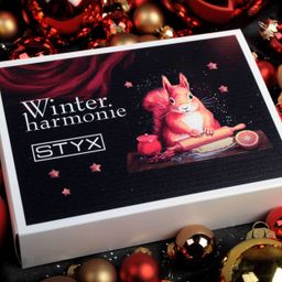 Eine weiße Box mit dem Markennamen STYX. Die Box enthält ein Winterharmonie-Set. Die Box hat ein Bild von einem Eichhörnchen, das einen Nudelholz hält und eine Orange. Der Hintergrund ist dunkel und es gibt Sterne und Ornamente.
