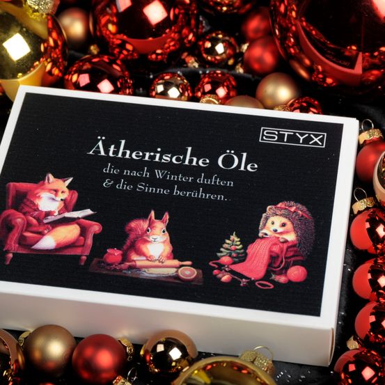 Eine Schachtel STYX ätherisches Öl mit Wintertieren, umgeben von roten und goldenen Weihnachtskugeln.