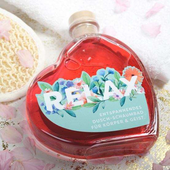Eine herzförmige Flasche mit roter Flüssigkeit, beschriftet mit 'RELAX' und Blumendesign, umgeben von Blütenblättern auf einem weißen Tuch.