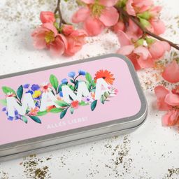 Eine rosafarbene Dose mit Blumenmustern zeigt in weißen Buchstaben 'MAMA'. Rosa Blumen sind umher verstreut.