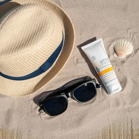 Ein Strohhut, Sonnenbrille und Sonnencreme am Strand mit einer Muschel in der Nähe.
