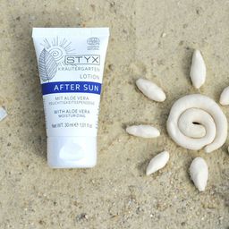 Eine weiße Tube mit der Aufschrift 'Styx After Sun' liegt auf Sand mit Muscheln. Die Tube enthält Aloe Vera und ist 30 ml groß.