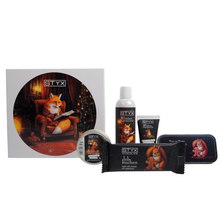 Das Bild zeigt ein STYX-Weihnachtsgeschenkset mit einem Fuchs und Winterelementen. Das Set besteht aus einer runden Kerze, einer Flasche, einem Röhrchen, einer Schokoladentafel und einer Blechdose. Die Verpackung und die Artikel sind mit Wintermotiven verziert.