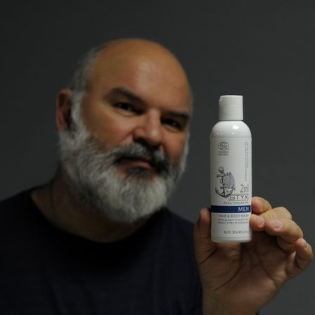 Ein Mann mit Bart hält eine Flasche STYX 2in1 Haar- und Körpershampoo.