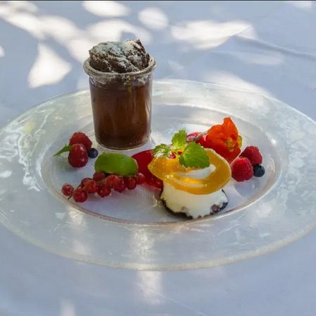 Ein Dessert auf einem Teller mit Schokoladenmousse, Beeren und Obst auf einer weißen Tischdecke.