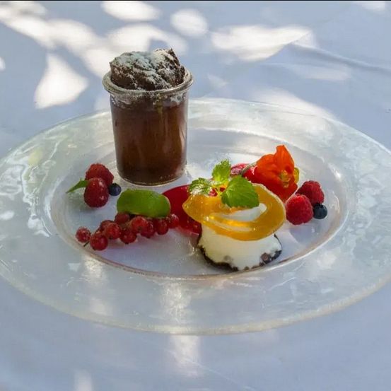 Ein Dessert auf einem Teller mit Schokoladenmousse, Beeren und Obst auf einer weißen Tischdecke.