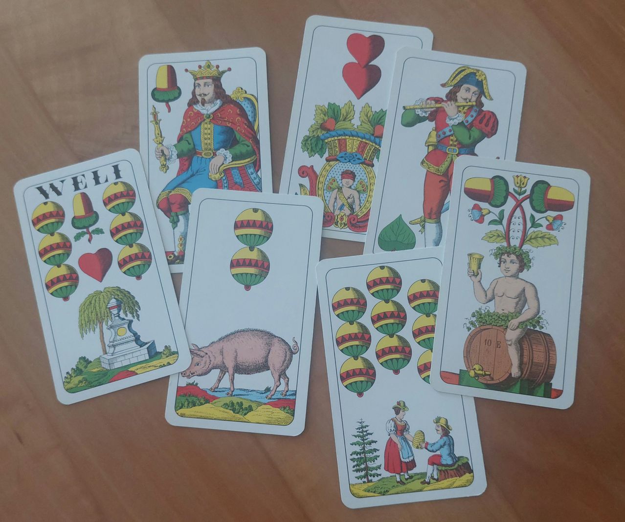 Several playing cards are laid out on a wooden table. The cards feature various illustrations such as a king, a pig, and a man playing the flute.