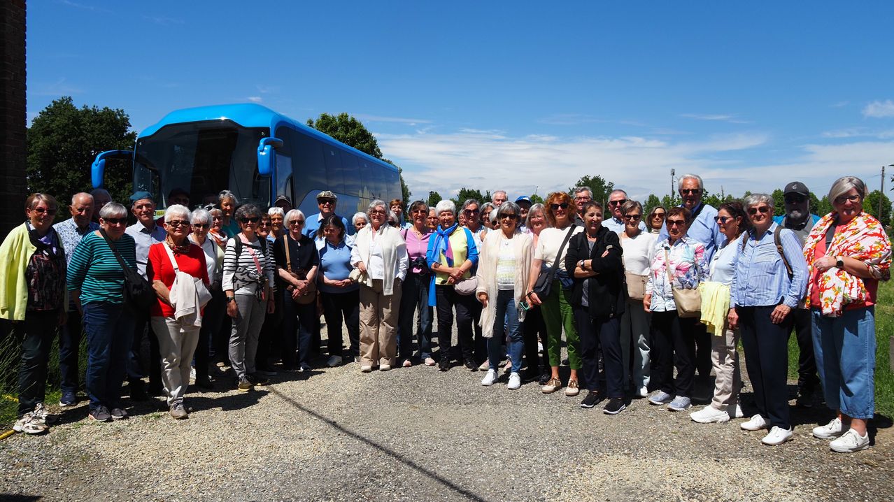 Eine Gruppe von Erwachsenen steht draußen vor einem blauen Bus an einem sonnigen Tag mit klarem Himmel.