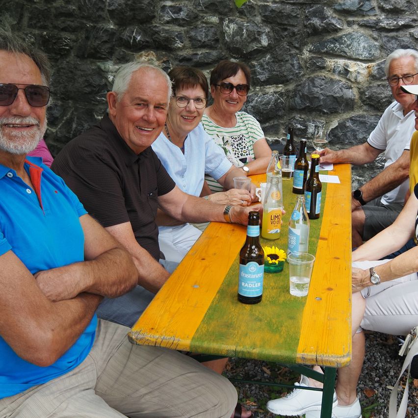 Eine Gruppe älterer Erwachsener sitzt um einen Tisch mit Flaschen und Gläsern, lächelt und posiert für ein Foto.