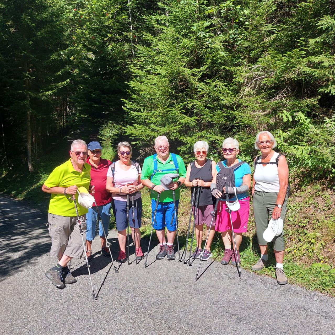 Eine Gruppe älterer Wanderer mit Stöcken posiert für ein Foto auf einem Waldweg.