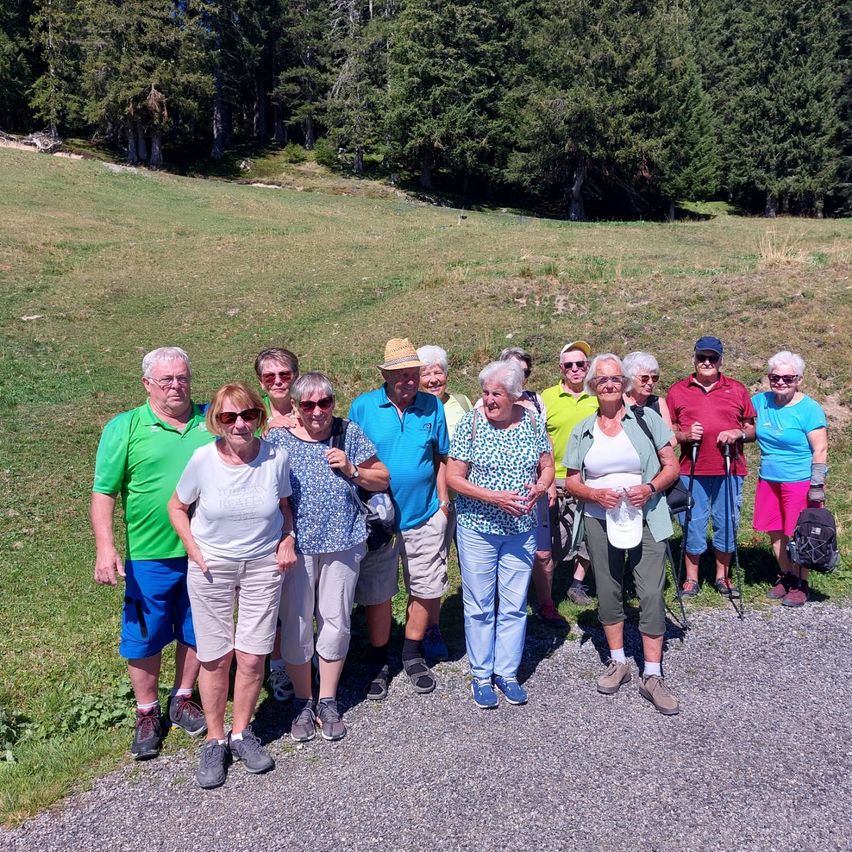 Eine Gruppe älterer Wanderer, in Freizeitkleidung gekleidet, posiert für ein Foto auf einem Kiesweg mit einem grasigen Hügel im Hintergrund.