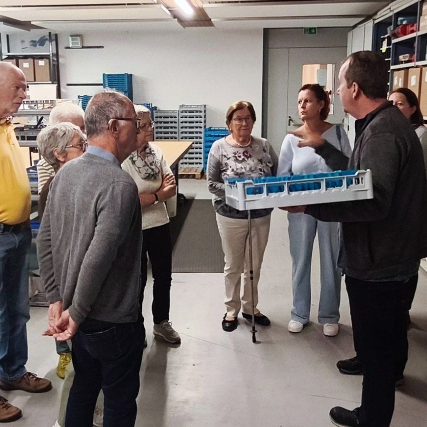 Eine Gruppe von Menschen in einem Raum, ein Mann hält eine Schale mit blauen Gegenständen, andere beobachten.
