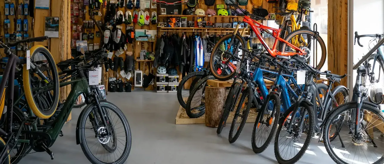 Ein Fahrradladen mit Holzwänden, der verschiedene Fahrräder, Helme und andere Fahrradausrüstung präsentiert. Der Laden ist gut organisiert, mit mehreren Fahrrädern in einer Reihe geparkt und einer Vielzahl von Zubehör, das an der Wand hängt.