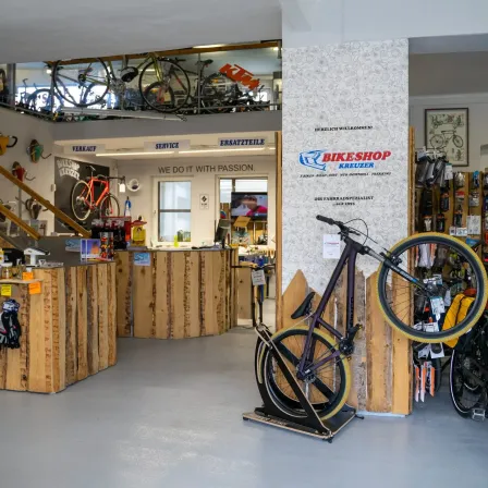 Ein Fahrradgeschäft mit hölzernen Theken, ausgestellten Fahrrädern und einem Schild, das 'Wir tun es mit Leidenschaft' besagt. Ein Fahrrad steht auf einem Ständer vor einer Wand.