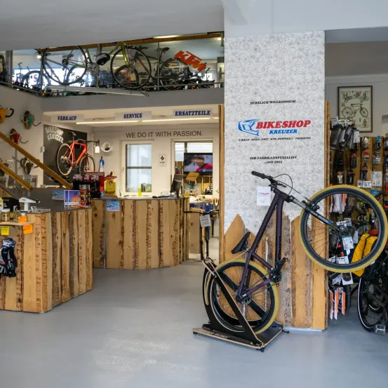 Ein Fahrradgeschäft mit hölzernen Theken, ausgestellten Fahrrädern und einem Schild, das 'Wir tun es mit Leidenschaft' besagt. Ein Fahrrad steht auf einem Ständer vor einer Wand.