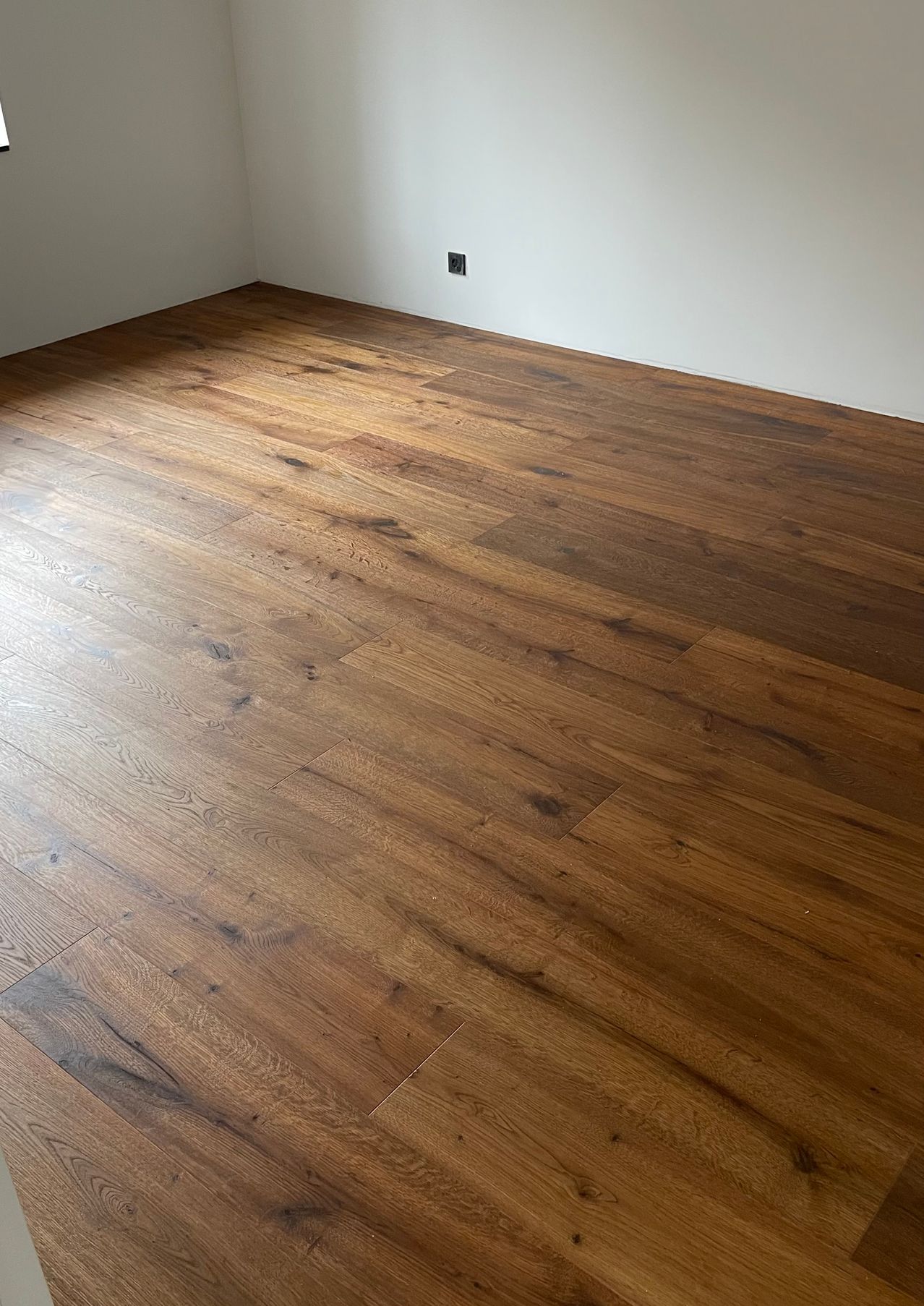 Ein leerer Raum mit Holzböden und weißen Wänden, mit einer Steckdose an der rechten Seite.