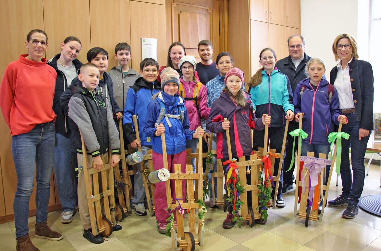 Eine Gruppe von Kindern, die mit Schleifen und Dekorationen verzierte Holzschlitten halten, steht in einer Reihe und lächelt für ein Foto.