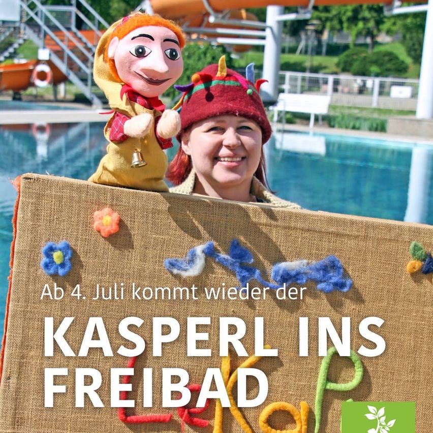 Eine Frau mit einer Puppe steht am Pool mit einem Schild, das 'Kasperl im Freibad' und den 4. Juli anzeigt. Die Frau lächelt und die Puppe trägt Hut und Schal. Im Hintergrund ist eine Wasserrutsche zu sehen.