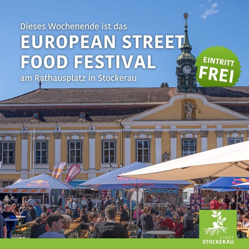 Am Rathausplatz in Stockerau findet ein Europäisches Street Food Festival statt, an dem viele Menschen unter Schirmen teilnehmen. Das Rathaus hat einen Glockenturm.