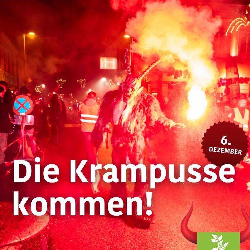 Eine Krampusfigur mit spitzem Hornhelm und rotem Pelz steht auf der Straße, eine Fackel in der Hand, umgeben von einer Menge. Das Bild ist in rotes Licht getaucht, mit einer festlichen Atmosphäre.
