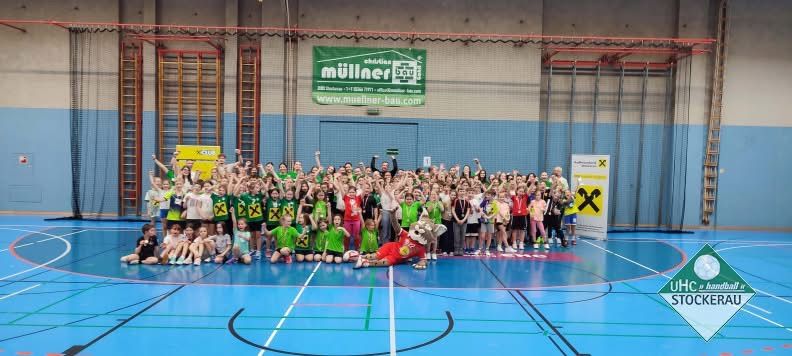 Eine Gruppenaufnahme von jungen Leuten in Sportausrüstung, die für ein Foto in einer Sporthalle mit einem Maskottchen in der Mitte posieren.
