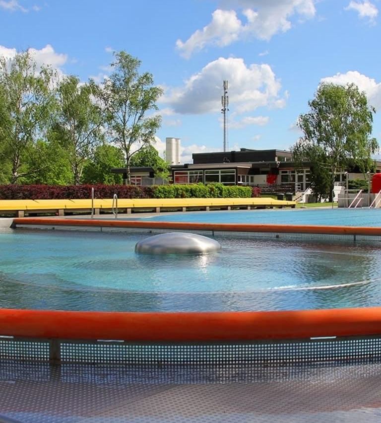 Ein großer runder Pool mit einem Metallrand und einer großen Kuppel in der Mitte. Bäume, Büsche und ein Gebäude im Hintergrund.