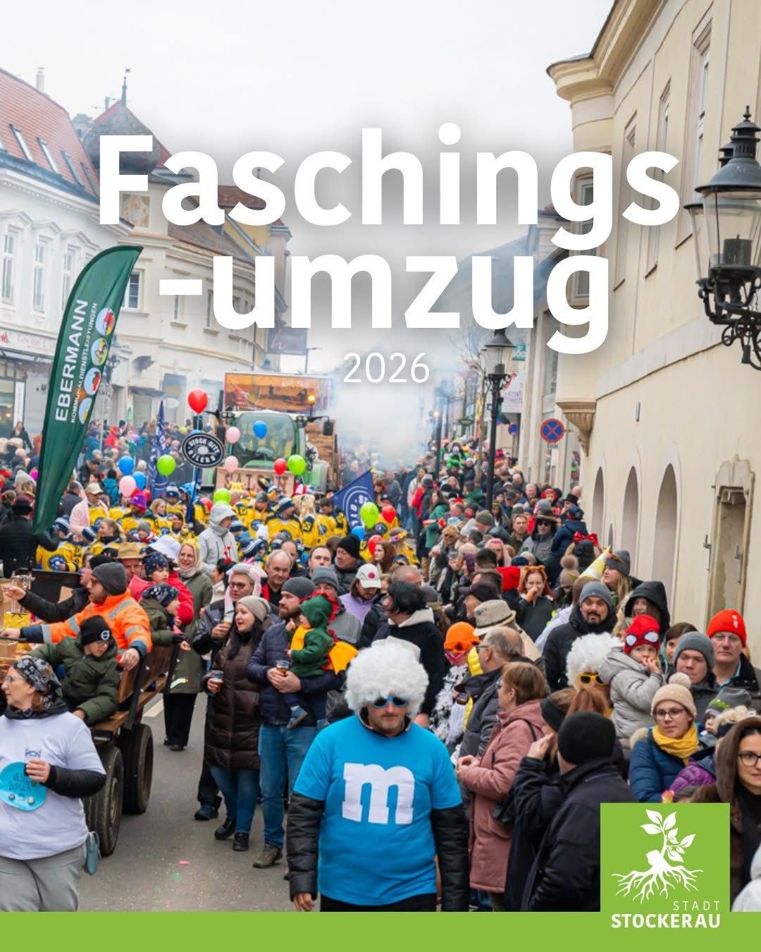 Eine große Menschenmenge versammelt sich im Freien für ein Fest. Viele tragen Kostüme, Hüte und halten Luftballons. Das Jahr 2026 ist prominent in Weiß angezeigt.