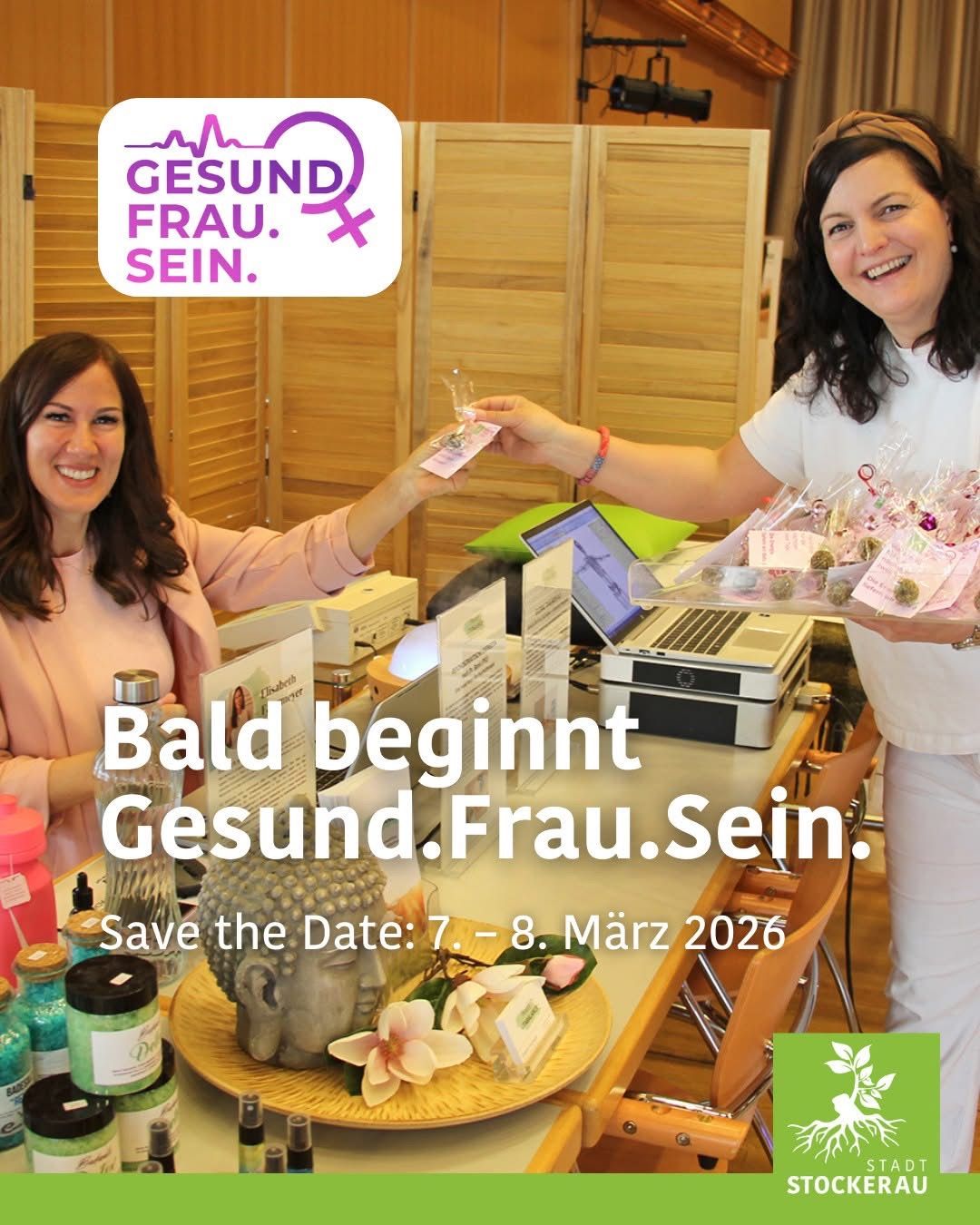 Zwei Frauen lächeln, eine reicht der anderen ein kleines Objekt. Sie stehen hinter einem Tisch mit einem Laptop, einem Drucker und verschiedenen Produkten. Ein Schild auf Deutsch lautet 'Bald beginnt Gesund.Frau.Sein.' Der Termin '7. - 8. März 2026' ist ebenfalls angezeigt.