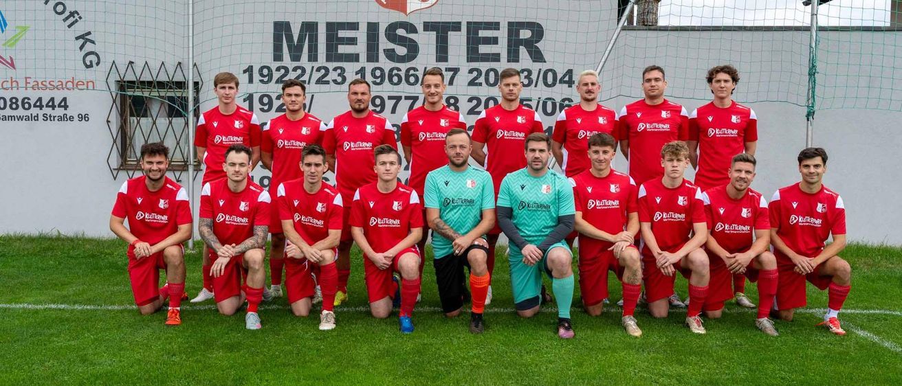 Eine Fußballmannschaft in roten Trikots posiert für ein Foto vor einer Wand mit dem Wort Meister.